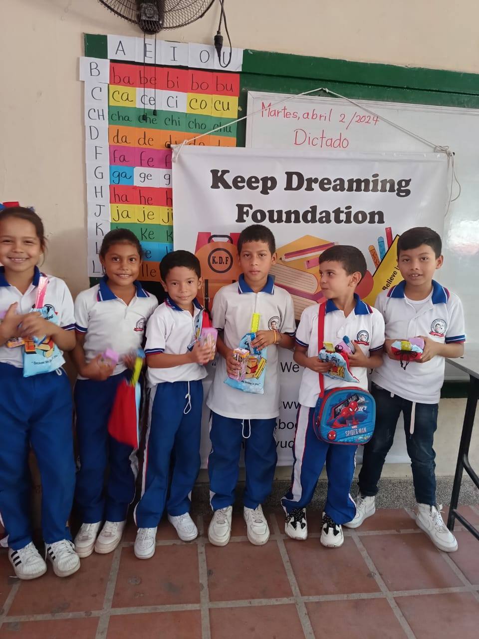 The KDF co-leader with six children in front of the Keep Dreaming Foundation banner, holding their gift bags