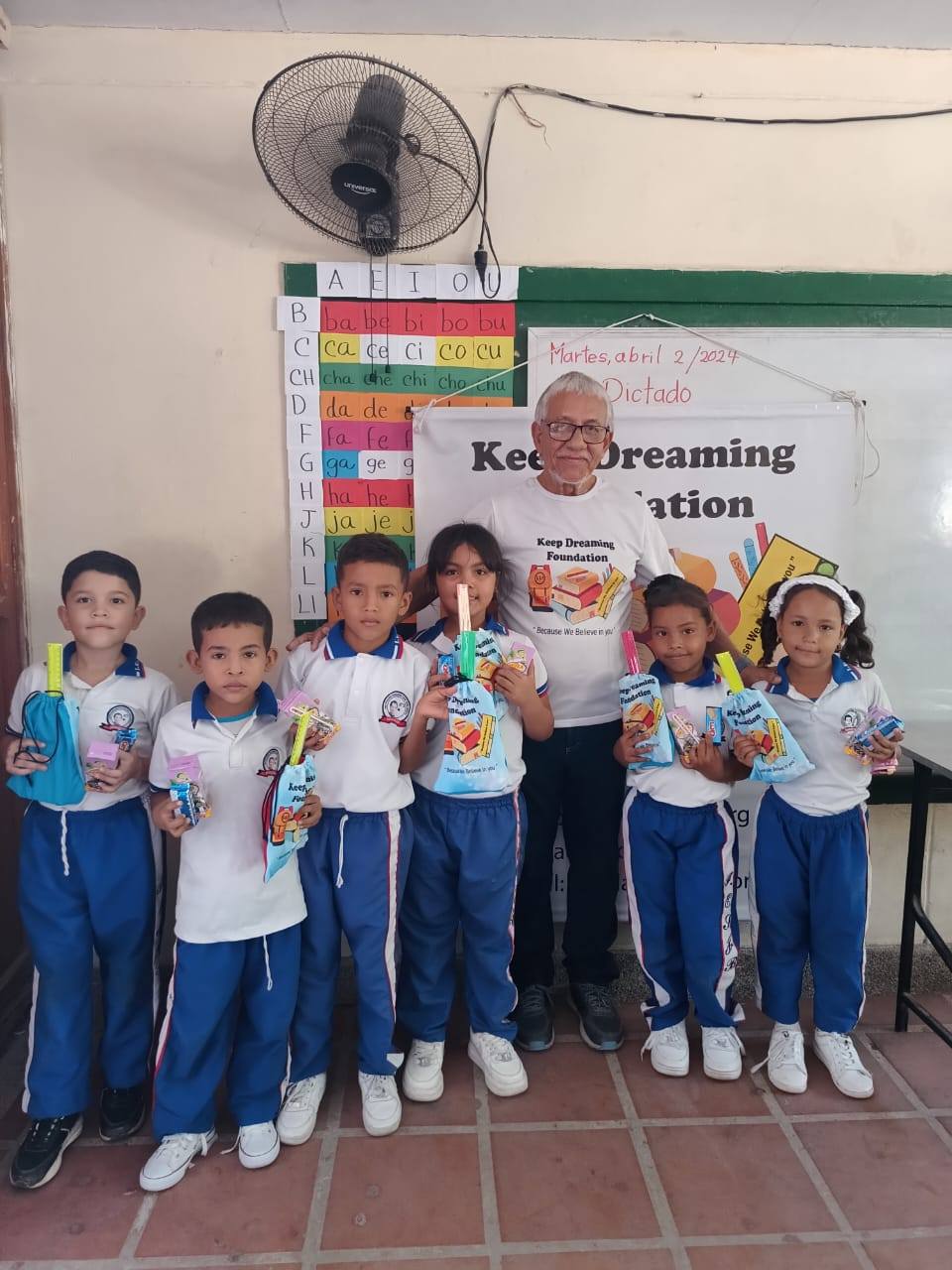 Seven Colombian schoolchildren posing with their KDF gift bags in front of the foundation banner