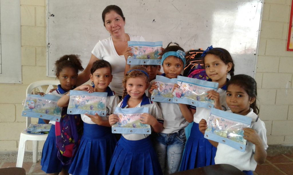 A group of girls in white school shirts and blue pleated skirts gathered around Marta in July 2017, each holding a decorated pencil pouch