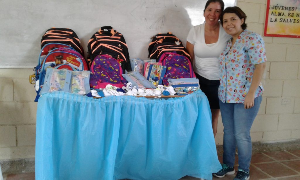 Marta and Liseth behind the very first distribution table in July 2017, loaded with orange backpacks, pencil pouches, socks and notebooks